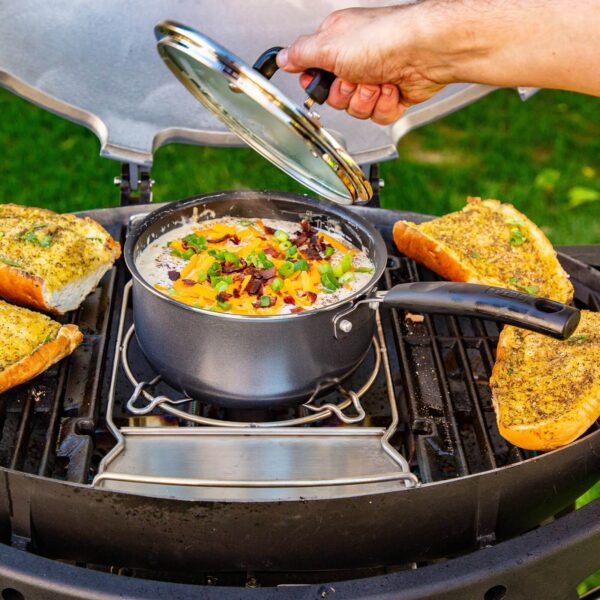 Cocinando sopa en una olla sobre el trébede de la barbacoa Pit Boss Sportsman 3, acompañada de pan de ajo en la parrilla.