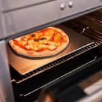 Pizza horneándose en una piedra de acero inoxidable Ooni dentro de un horno doméstico.