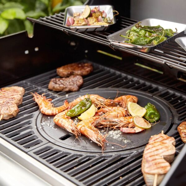 Alimentos variados cocinándose en una barbacoa Landmann, incluyendo camarones, carne, pimientos y verduras en la plancha reversible.