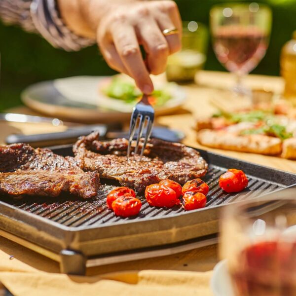 Plancha de doble cara de hierro fundido Ooni con asas y trípode sobre fondo neutro, ideal para asar y cocinar al aire libre.