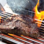 Carne asándose en la parrilla con llamas y humo visible.