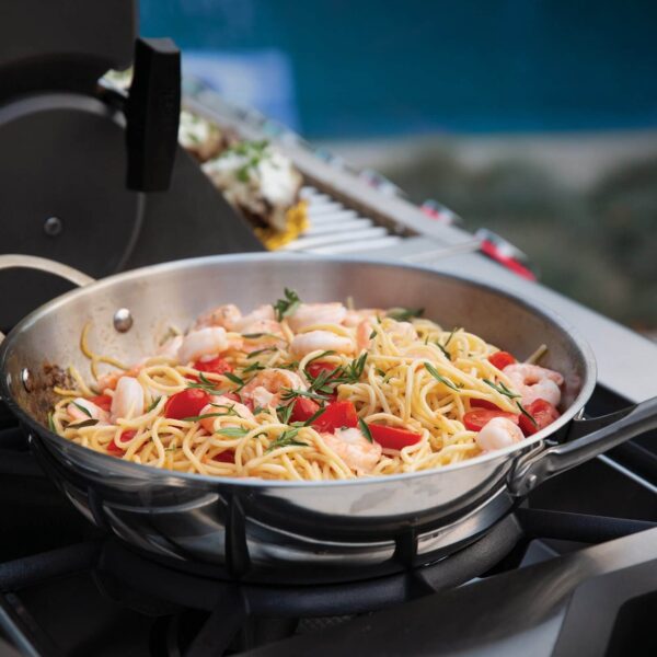 Plato de espaguetis con camarones y tomates cocinándose en un wok de acero inoxidable sobre una estufa de gas al aire libre.