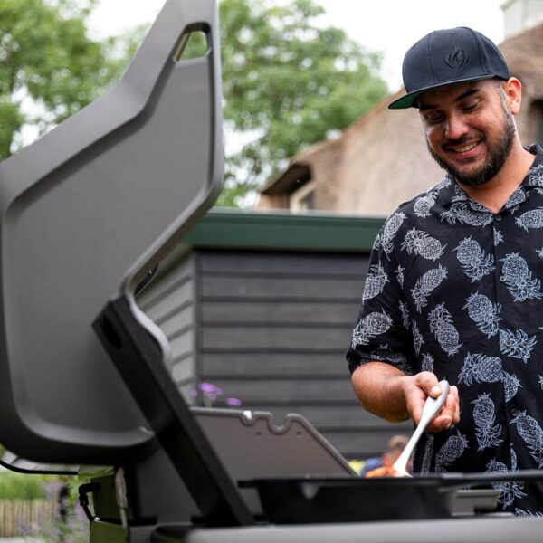 Hombre sonriendo mientras cocina en la parrilla Napoleon Rogue 425 en un entorno al aire libre.