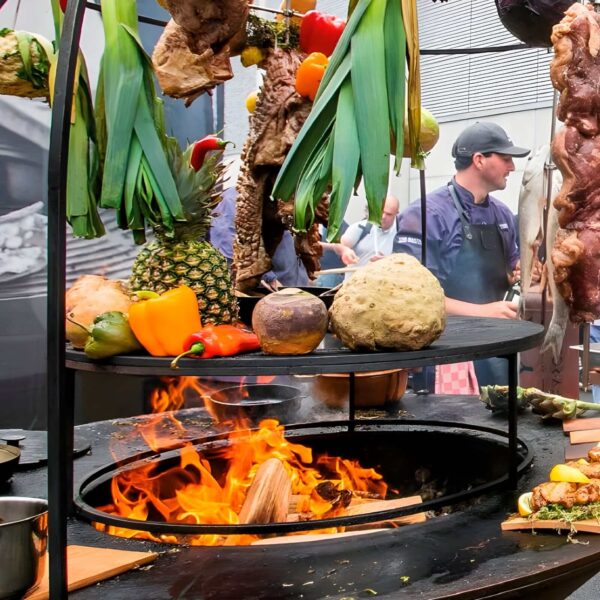 Set de Ampliación XL OFYR con alimentos colgando y cocinándose al fuego en un evento al aire libre.