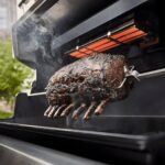 Costillar de res cocinándose en el rustidor giratorio de la barbacoa Weber Summit FS38 E, bajo un grill de infrarrojos.