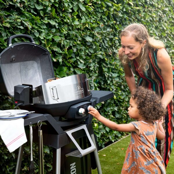 Niña pequeña ayudando a su madre a cocinar en una barbacoa Napoleon TravelQ en el jardín.