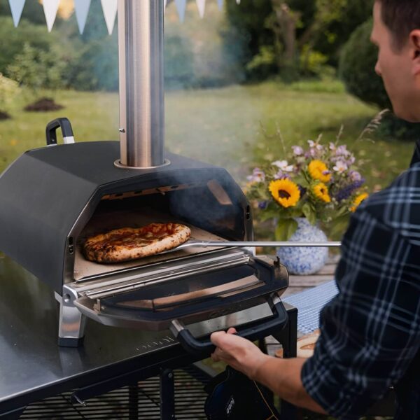 Persona retirando una pizza cocida en el horno Ooni Karu 16 en un jardín.