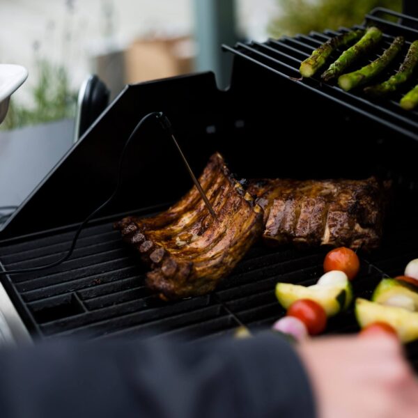 Una parrilla de asado mostrando costillas perfectamente cocidas con un termómetro digital Landmann asegurando la cocción ideal.