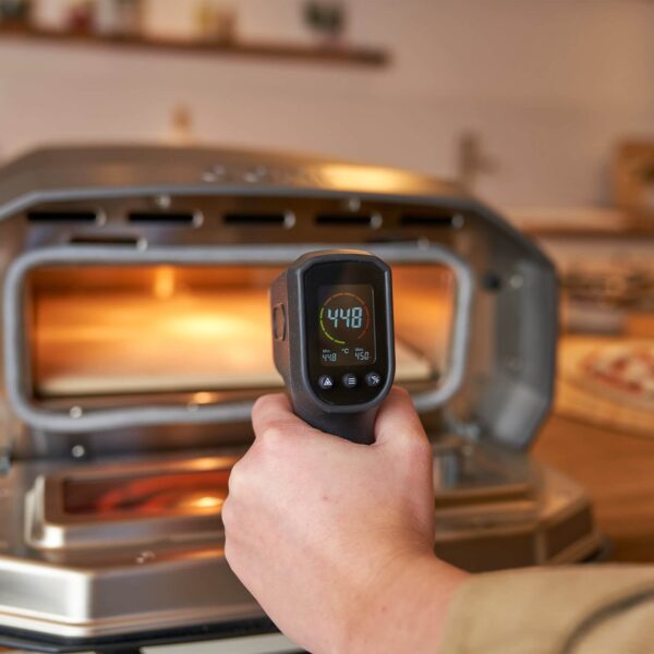 Mano utilizando el termómetro infrarrojo digital Ooni para medir la temperatura en el horno de pizza.