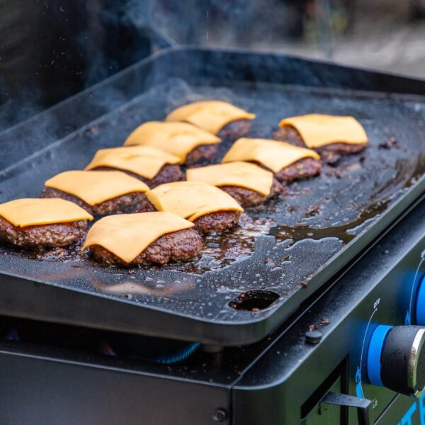 Jugosas hamburguesas con queso cheddar cocinándose en la plancha Pit Boss.