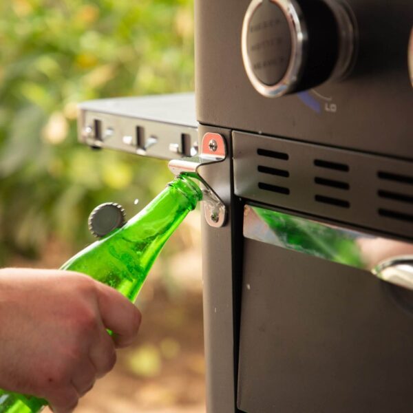 Mano usando el abridor de botellas incorporado en la plancha de cocina Pit Boss.