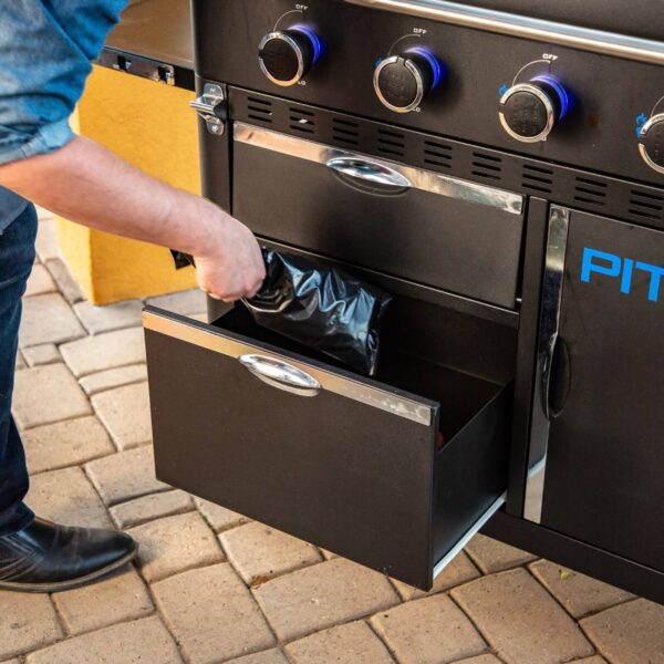 Persona abriendo el cajón inferior de una plancha de cocina Pit Boss para revelar una bolsa de basura negra.