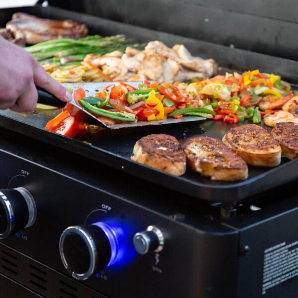 Detalle de alimentos siendo cocinados en la plancha de cocina Pit Boss, con enfoque en los colores vibrantes de los vegetales y mariscos.