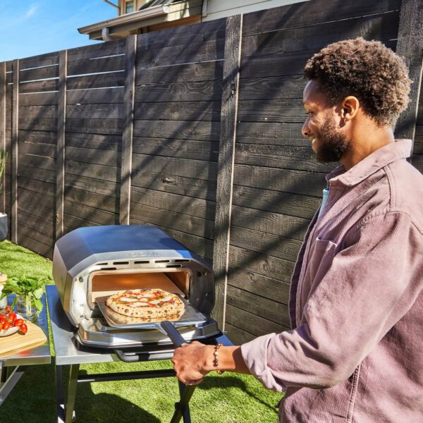 Persona utilizando el horno de pizza Ooni Volt 12 al aire libre para cocinar una pizza fresca.