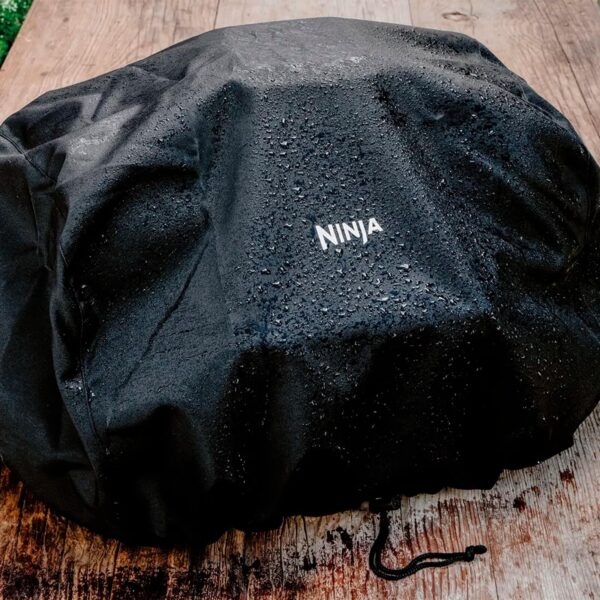 Funda negra impermeable Ninja cubriendo una parrilla, con gotas de agua en la superficie.