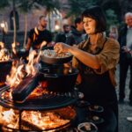Mujer cocinando con cazuelas de hierro fundido sobre una parrilla OFYR durante una reunión al aire libre.