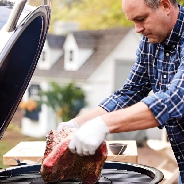 Hombre colocando un gran trozo de carne en la barbacoa Summit® Kamado S6 al aire libre.