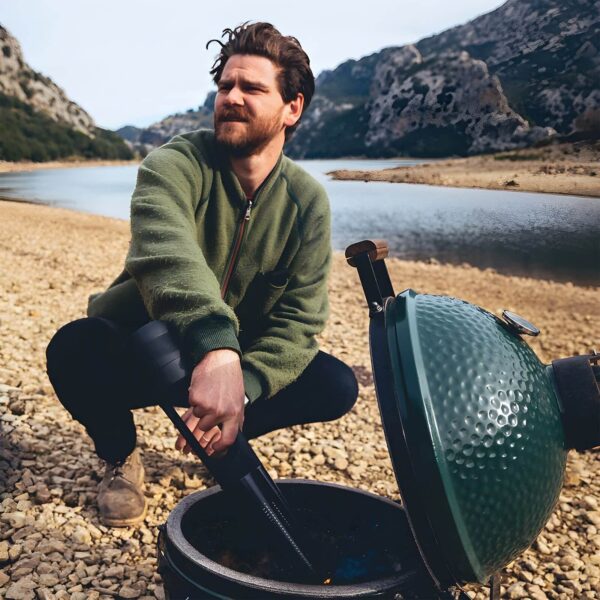 Hombre encendiendo carbón en una barbacoa Kamado con el encendedor eléctrico Looft Lighter X, junto a un lago y montañas de fondo.