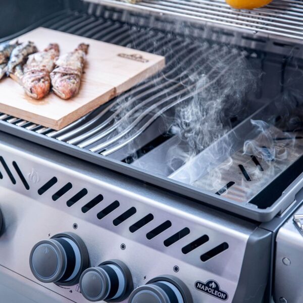 Caja de ahumado Napoleon en acción en una barbacoa, con humo aromático impregnando unas jugosas piernas de pollo.