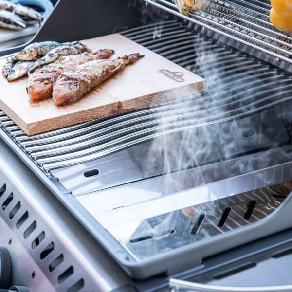 Primer plano de la caja de ahumado Napoleon en uso con pescado y carne cocinándose al lado en una barbacoa de acero inoxidable.