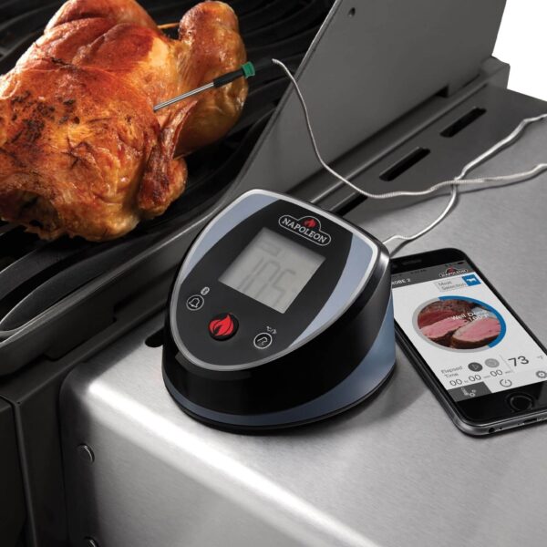 La Sonda Digital Accu-Probe Bluetooth en uso en una barbacoa, monitoreando la temperatura de un pollo asado, con un smartphone mostrando la aplicación a un lado.