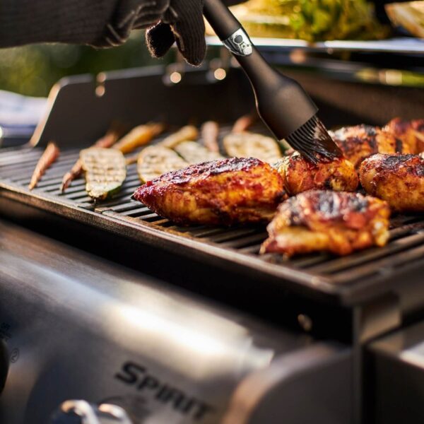 Persona marinando pollo a la parrilla en una barbacoa de gas Weber Spirit E-215 GBS con verduras asándose.