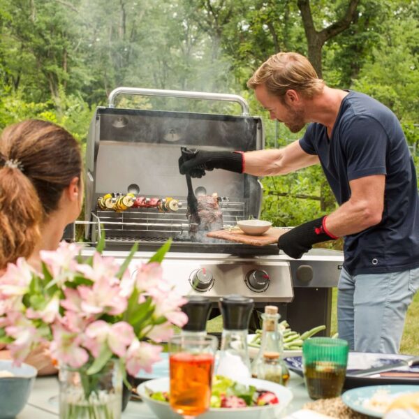 Hombre cocinando carne y brochetas en una barbacoa Weber Genesis II E-310 GBS mientras una mujer observa