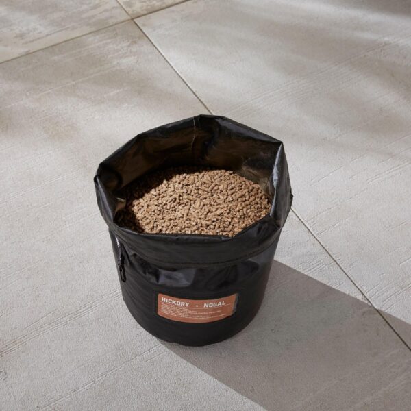 Bolsa de almacenamiento Weber con pellets de Hickory Nogal en su interior, ubicada en una superficie exterior.