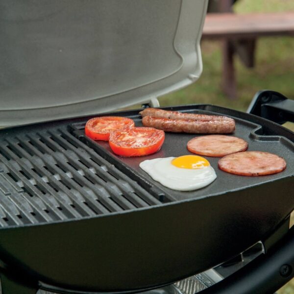 Desayuno cocinándose en una barbacoa Weber con la Plancha de Hierro Colado Q 1000, incluyendo salchichas, tomate, jamón y huevo frito.