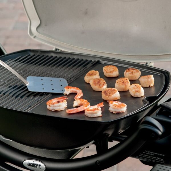 Camarones y vieiras cocinándose en la plancha de hierro colado Q 2000 de Weber, con una espátula de metal en la parrilla.