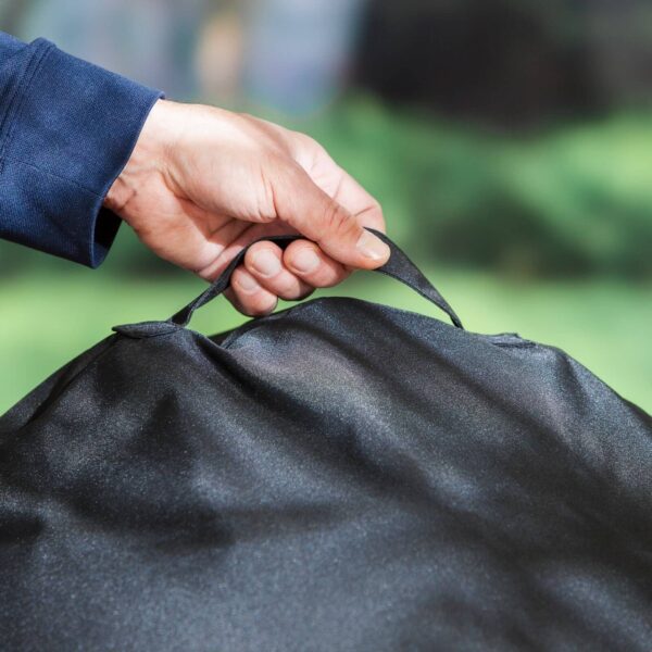 Mano sujetando el asa de la Funda Premium para barbacoa de 57 cm, mostrando la facilidad de uso y transporte.