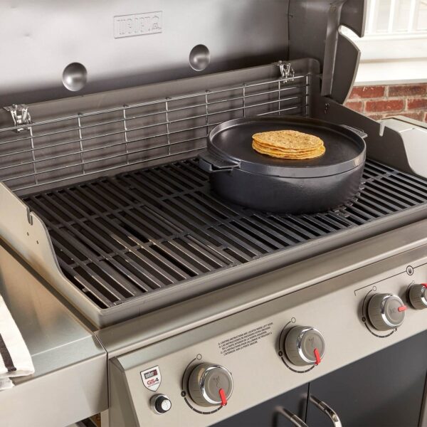 La imagen muestra una barbacoa Weber con la olla de hierro colado, en la cual se utiliza la tapa como plancha para cocinar panes. Esta escena destaca la versatilidad del diseño 2 en 1, permitiendo tanto la cocción directa dentro de la olla como el uso de la tapa para asar alimentos. Ideal para aprovechar al máximo el espacio y la funcionalidad durante las barbacoas al aire libre.