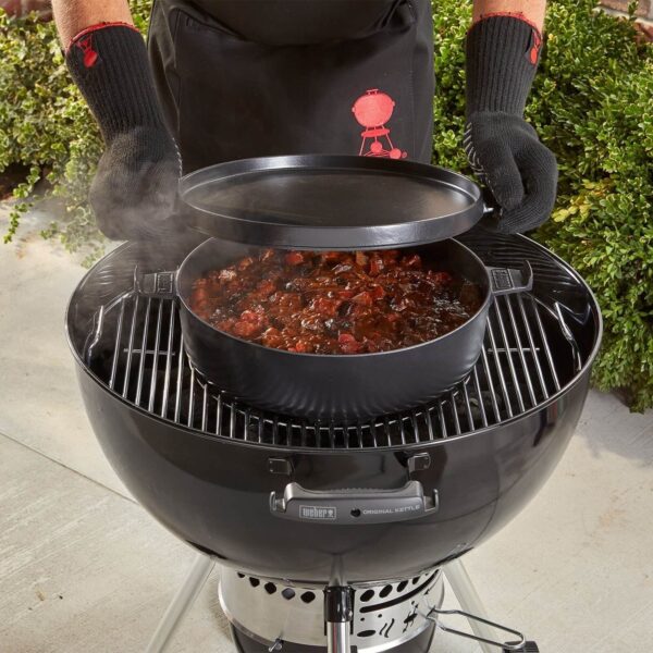 Persona levantando la tapa plana de una olla de Hierro Colado Weber en una barbacoa, mostrando un guiso cocinándose.