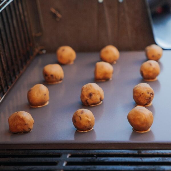 Bolas de masa para galletas colocadas sobre la piedra para pizza esmaltada de Weber en una barbacoa.