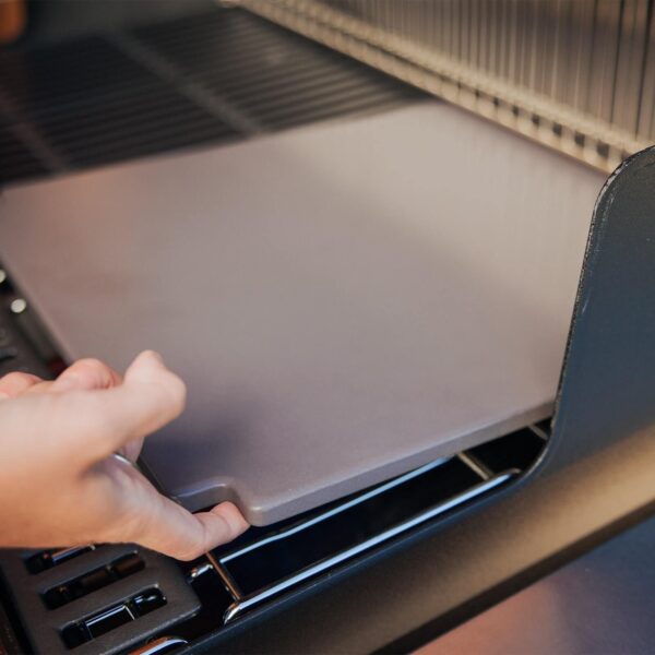 Persona instalando la piedra para pizza esmaltada de Weber en una barbacoa, mostrando su fácil colocación.