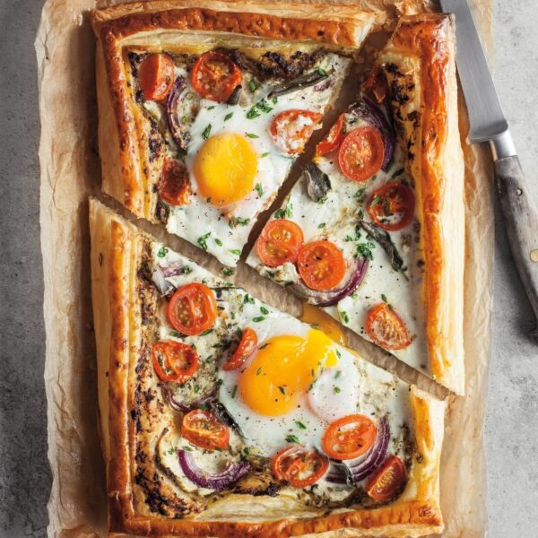 Tarta salada de hojaldre con huevos, tomates cherry y cebolla morada, recién horneada y cortada en porciones.