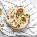 Pan naan casero con ajo y cilantro, apilado en un plato sobre un paño de cocina.