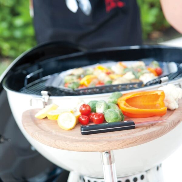 Preparación de verduras en cesta Weber sobre una barbacoa kettle, con un cocinero al fondo.