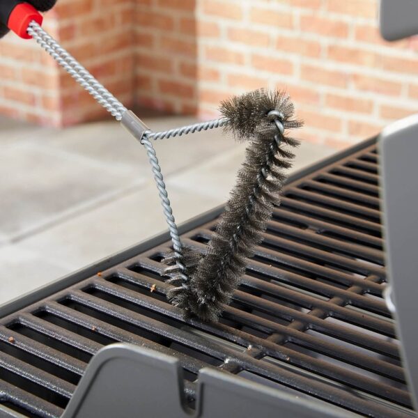 Cepillo en T Weber limpiando una rejilla de parrilla con cerdas metálicas.