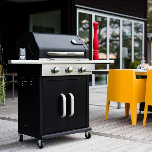 Parrilla de gas negra con accesorios en una terraza al aire libre junto a muebles modernos.