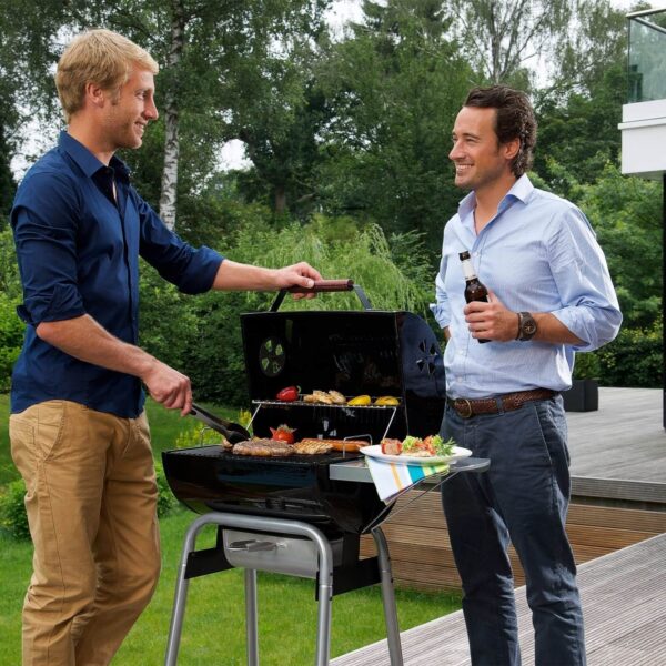 Dos hombres disfrutando de una reunión al aire libre con una barbacoa Black Taurus 440, cocinando una variedad de carnes y vegetales