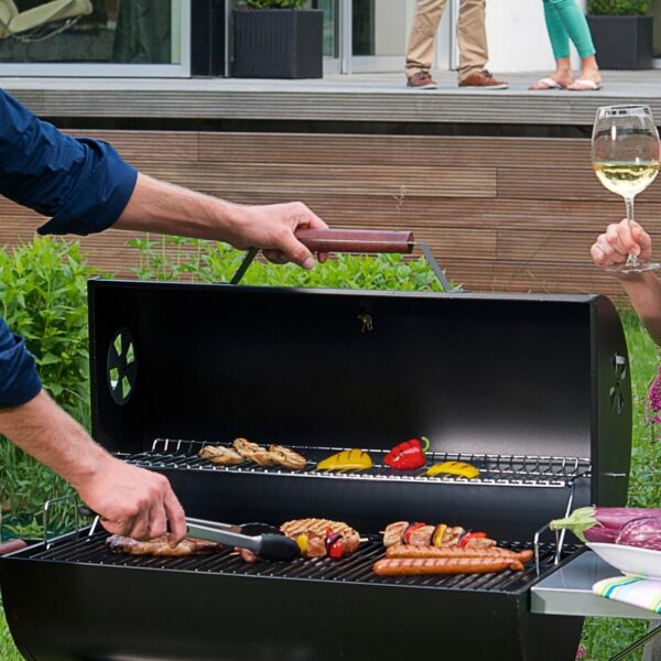 Personas disfrutando de un asado al aire libre con la barbacoa LANDMANN Black Taurus 660, destacando la interacción social alrededor de la comida