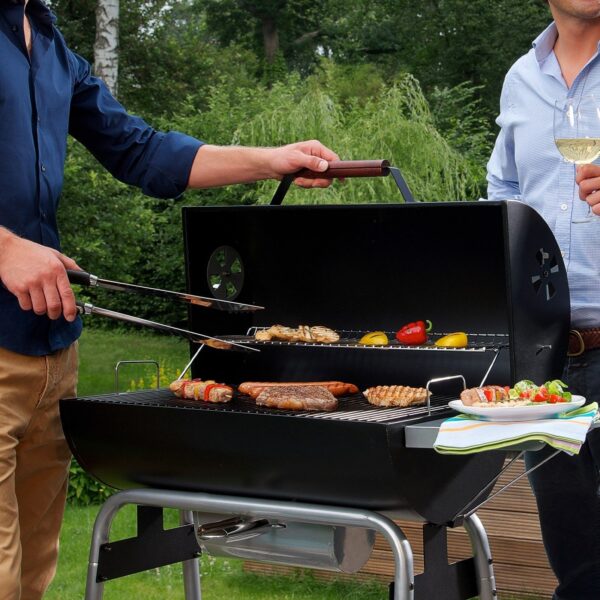 Amigos cocinando y disfrutando juntos alrededor de una barbacoa LANDMANN Black Taurus 660 en un jardín.