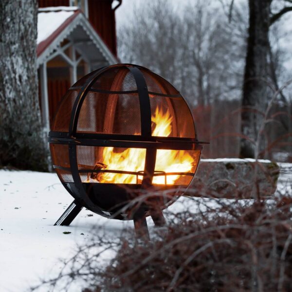 Brasero Bola de Fuego encendido en un jardín nevado al atardecer, proporcionando un cálido refugio invernal.