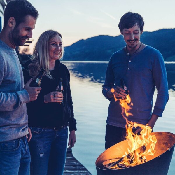 Grupo de amigos compartiendo historias junto a una cesta de fuego de Höfats a la orilla del lago al atardecer.