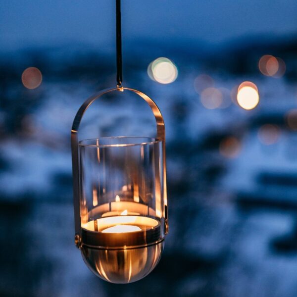 Un candelabro Gravity Candle colgante se destaca contra un fondo de cielo azul nocturno y luces borrosas de la ciudad, simbolizando tranquilidad y serenidad.