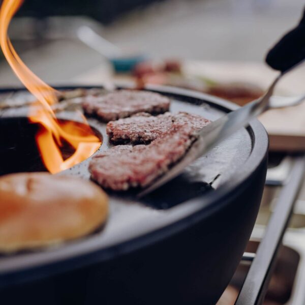 Llamas lamiendo las jugosas hamburguesas cocinándose en una parrilla al aire libre.