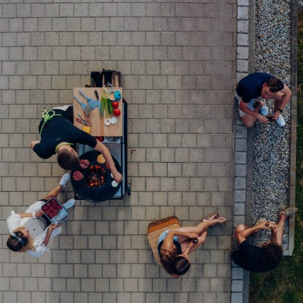 Vista aérea de amigos disfrutando de una sesión de cocina al aire libre con una estación de cocina moderna y parrilla de fuego.