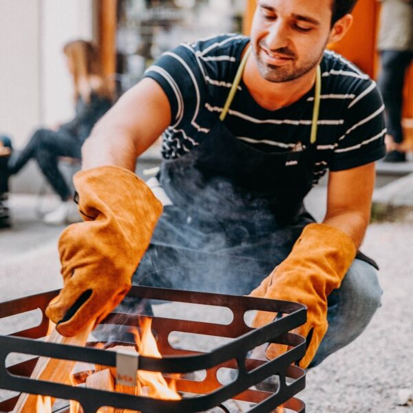 Hombre sonriendo mientras maneja una parrilla caliente con guantes Höfats.