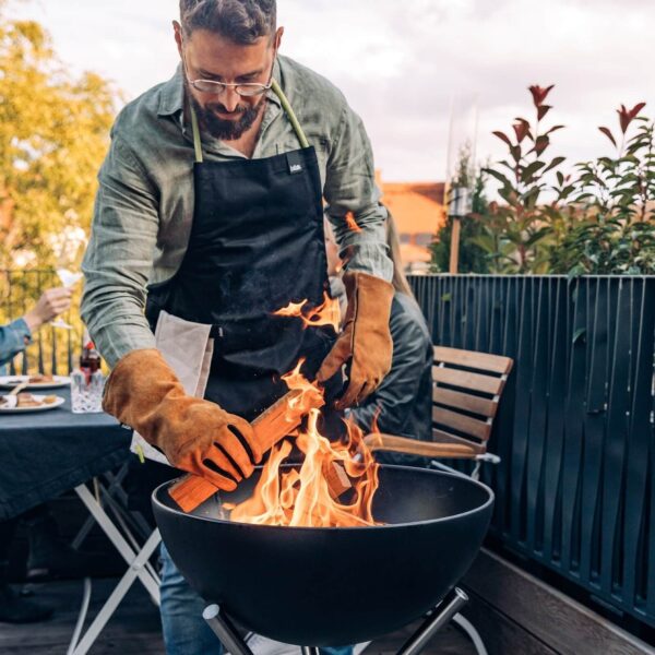 Hombre utilizando guantes Höfats para manejar el fuego en una barbacoa urbana.